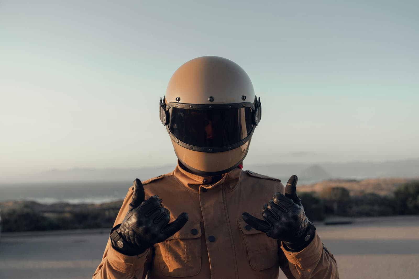 Motard en casque intégral, veste et gants de cuir, au bord de la mer