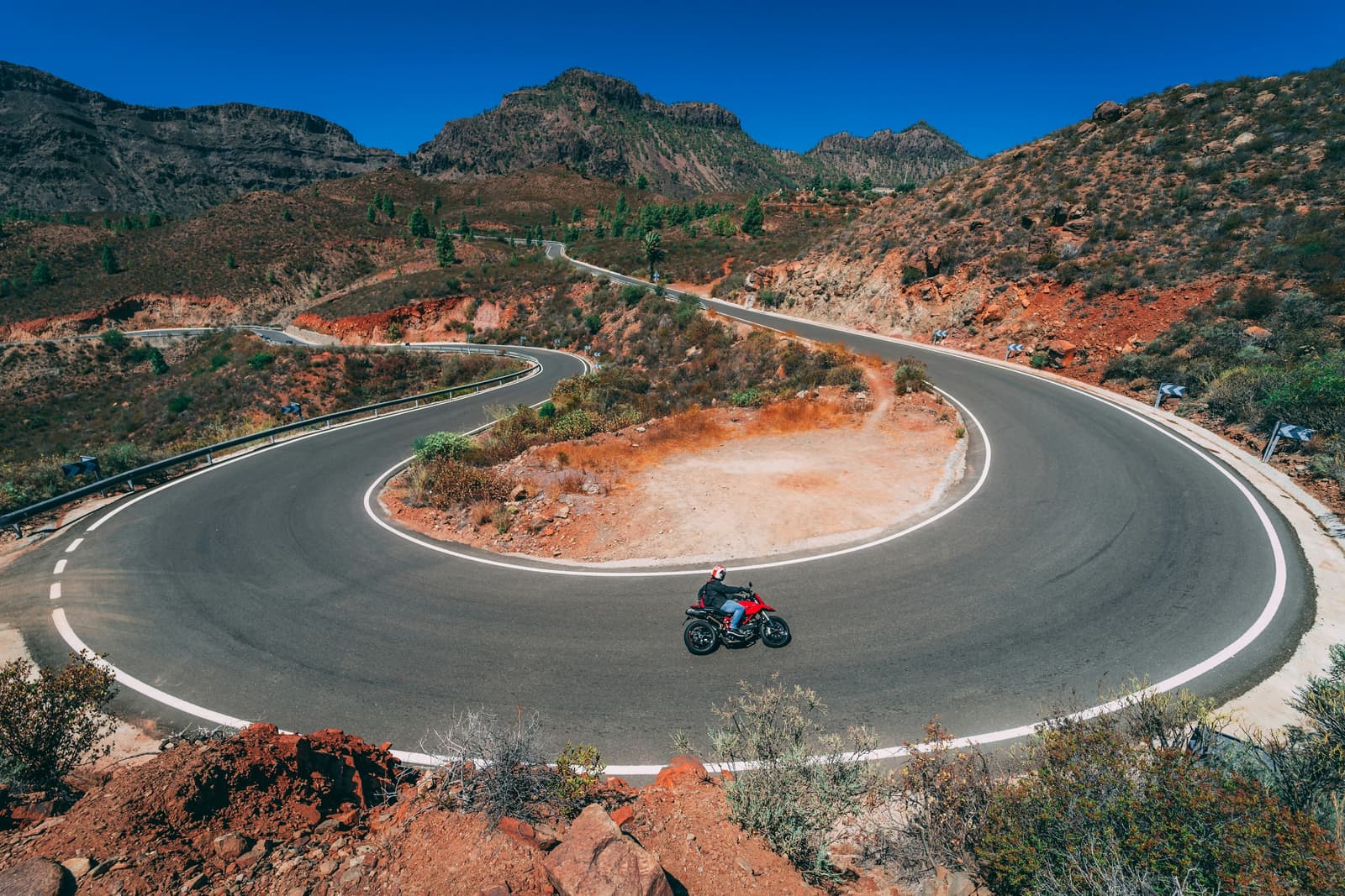 Rider on a red roadster in a hairpin bend, between red rocks and pines