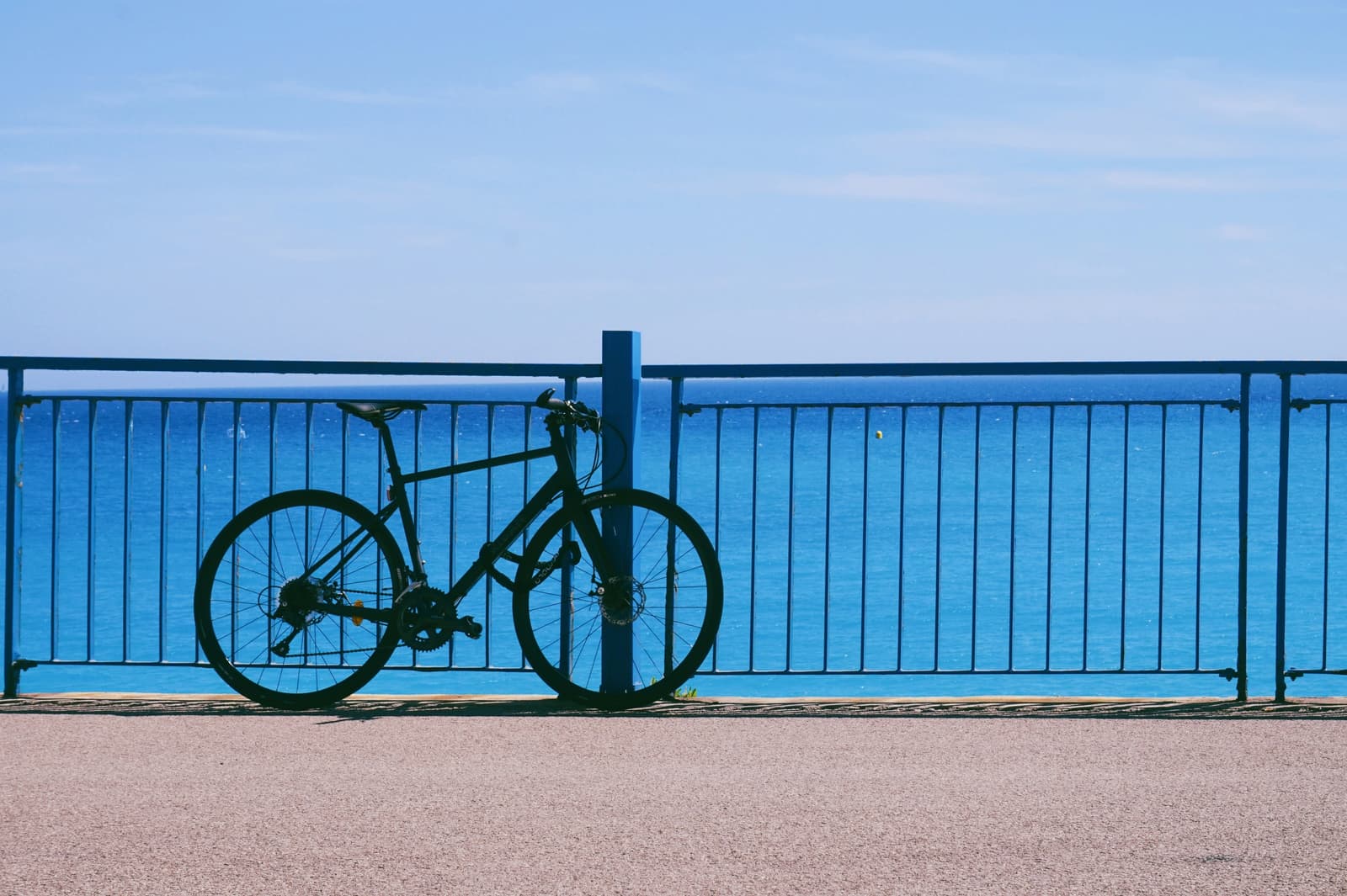 Vélo appuyé contre une rambarde bleue, face à la mer